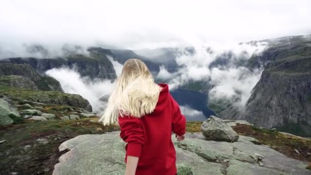 Een jong meisje met lange haren in een rode trui wandelingen in de bergen. Fjorden Noorwegen. — Stockvideo