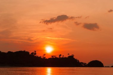 Altın gün batımına doğru bir ada silüeti denize sıfır. Güneş, gökyüzü, deniz, dalgalar ve kum