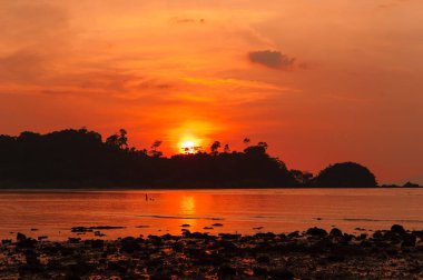 Altın gün batımına doğru bir ada silüeti denize sıfır. Güneş, gökyüzü, deniz, dalgalar ve kum