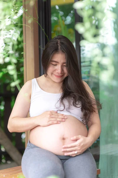 Femeia gravidă se simte fericită acasă în timp ce are grijă de copilul ei. Îngrijirea prenatală a maternității și conceptul de sarcină a femeii . — Fotografie, imagine de stoc