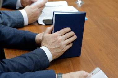 Elinde defter tutan takım elbiseli bir adamın elleri.