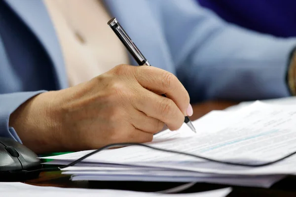 A woman\'s hand holds a fountain pen. Business papers and a laptop mouse are on the table