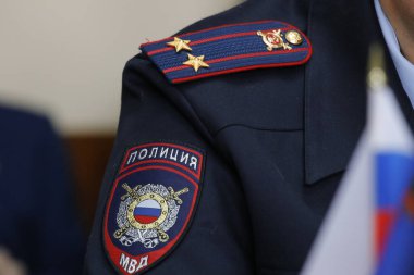Fotoğrafta bir Rus polis memurunun üniformasının kısmi görüntüsü var. Kolunda bir sembol ve kolunda Yarbay rütbesi olan bir omuz askısı var.