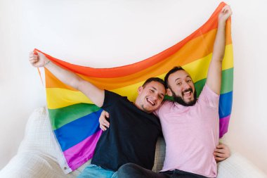 Birbirini tutan ve LGBTQ bayrağı taşıyan iki beyaz homoseksüel adamın stok fotoğrafı. Gülüyorlar..