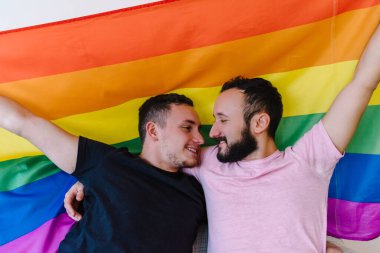 Birbirini tutan ve LGBTQ bayrağı taşıyan iki beyaz homoseksüel adamın stok fotoğrafı. Gözleri kapalı..