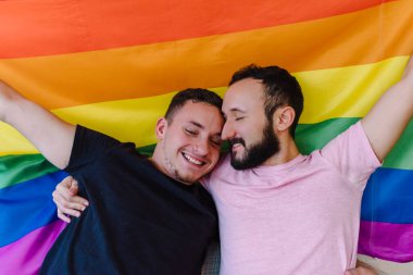 Birbirini tutan ve LGBTQ bayrağı taşıyan iki beyaz homoseksüel adamın stok fotoğrafı. Gözleri kapalı..