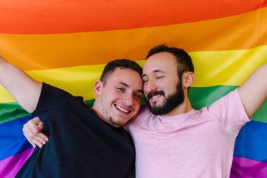 Birbirini tutan ve LGBTQ bayrağı taşıyan iki beyaz homoseksüel adamın stok fotoğrafı. Gözleri kapalı..