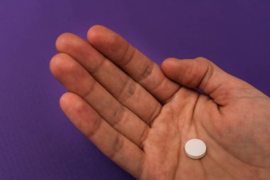 Mor arka planda birinin tek bir tableti çimdiklediğini gösteren bir fotoğraf. Bu kişi tanınmaz halde..