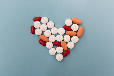 Kalp şeklinde mavi bir arka plana yerleştirilmiş bir sürü hapın stok fotoğrafı. Resimde kimse yok..