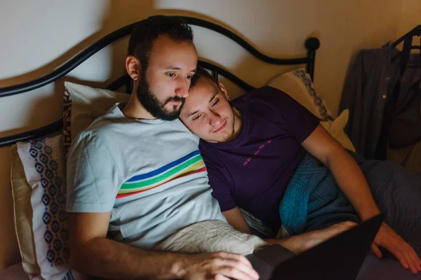 ベッドに座っている2人の同性愛者の白人男性のストック写真 彼らはラップトップで何かを見ています 抱っこしてる — ストック写真