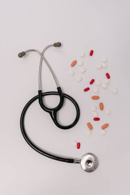 Beyaz arka planda farklı haplarla çevrili bir steteskopun stok fotoğrafı. Resimde kimse yok..