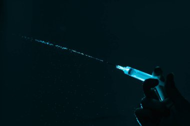 Karanlık arka planda su damlaları olan şırınga kullanan isimsiz bir kişi..