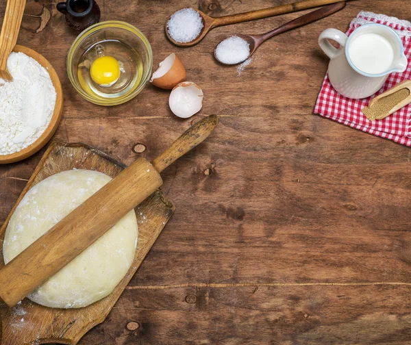 yeast dough from white flour and a wooden rolling pin on a brown board, copy space