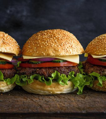 taze ev yapımı Hamburger marul, peynir, soğan ve domates karanlık bir arka plan üzerinde bir rustik ahşap tahta üzerinde Kapat