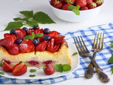 Süzme peynir ve yanındaki iki çatal beyaz bir seramik tabak taze çilek cheesecake