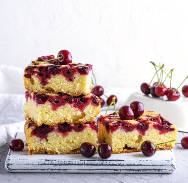 Beyaz ahşap bir tahtada, beyaz arka planda pişmiş kare kirazlı turta yığını.