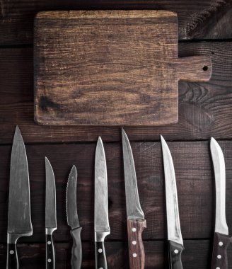 kullanılan mutfak bıçakları ve bir boş kahverengi ahşap kesme tahtası, üstten görünüm