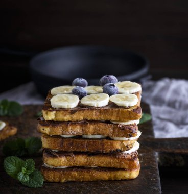 kare kızarmış ekmek dilimleri kahverengi ahşap masa, yumurtalı ekmek kahvaltıda çikolata ve muz dilimleri ile yığını