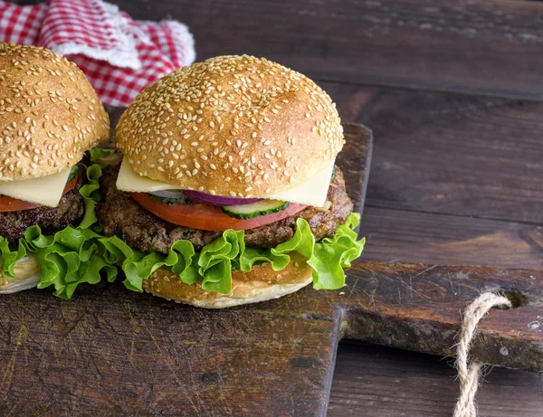 hamburger with a meat chop and a round bun with sesame on a brown wooden board