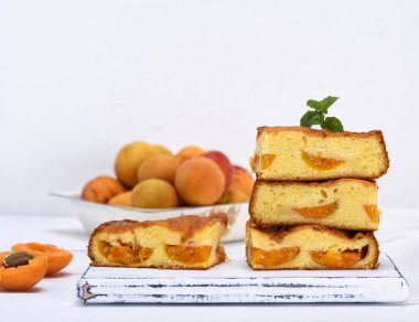 kare dilim kek sünger bir beyaz tahta masa, beyaz arka plan, kopya alanı üzerinde taze kayısı ile pişmiş