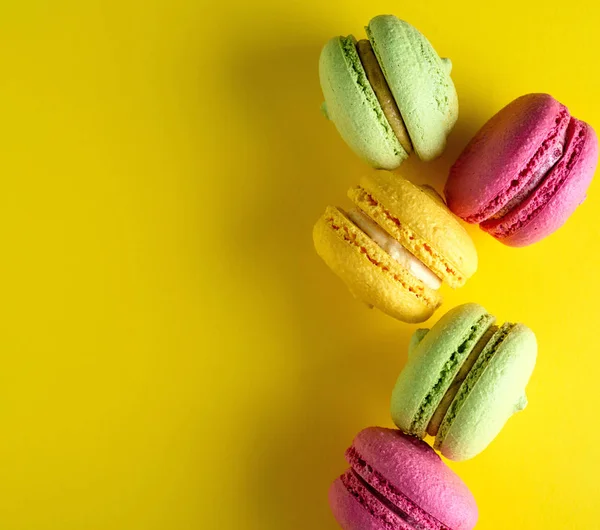 multi-colored round cakes with cream macarons on a yellow background, copy space