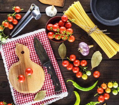 Ahşap kesme tahtası bir bıçak ve yanında uzun ham spagetti bağlı bir demet taze kırmızı kiraz domates ile