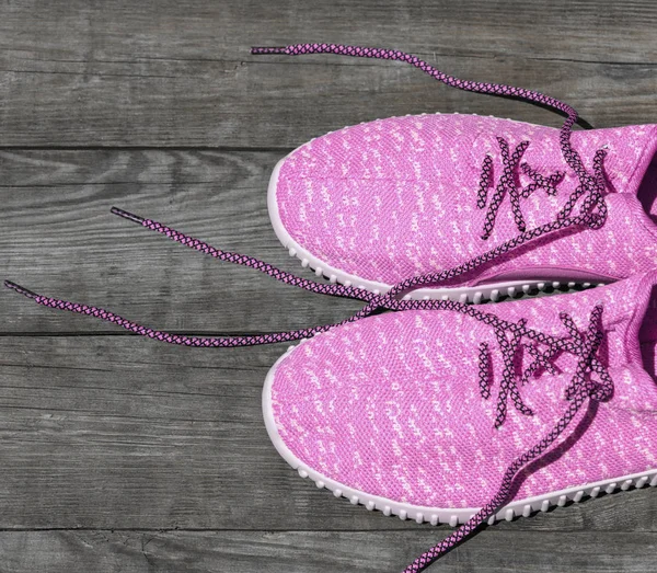 pink textile sneakers with untied laces on a gray background of wooden planks, top view