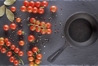 boş yuvarlak dökme demir tava ve taze kırmızı olgun kiraz domates siyah bir arka plan, üstten görünüm