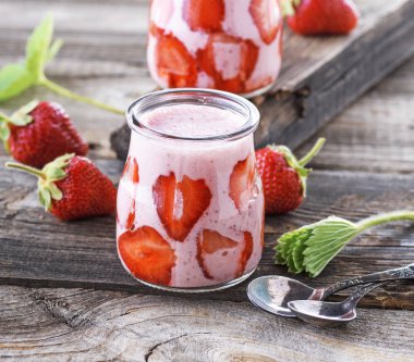 Olgun kırmızı çilek ve iki cam kavanoz smoothies gri bir ahşap masa üzerinde Kapat