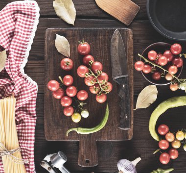 Ahşap kesme tahtası bir bıçak ve yanında uzun ham spagetti bağlı bir demet taze kırmızı kiraz domates ile