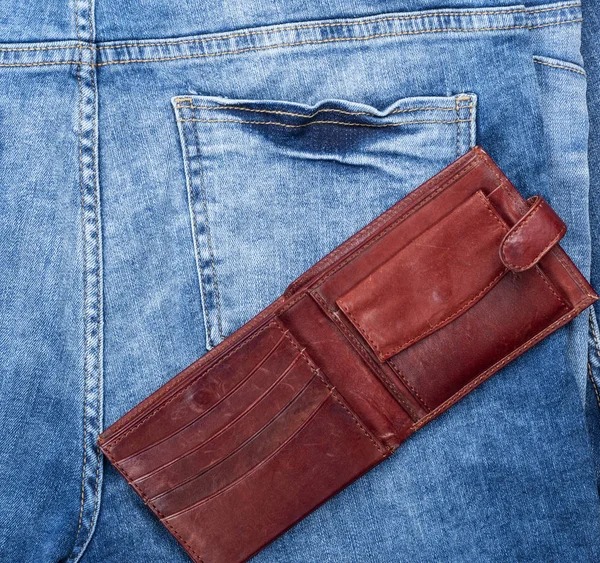ブルー ジーンズの背景で空の茶色の革財布を開く — ストック写真