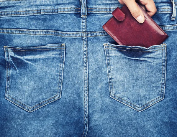 brown leather purse lies in the back pocket of blue jeans, a female hand clings to a purse