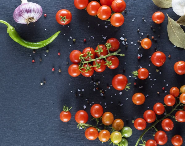 red cherry tomatoes on the twigs sprinkled with salt and pepper, black graphite background