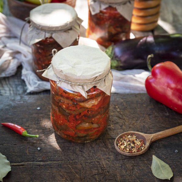 Canned eggplant slices in spicy vegetable sauce in glass jars on a wooden table, top view