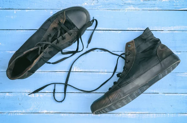 一对黑色破旧的运动鞋与松开鞋带在蓝色的木质背景 顶部视图 — 图库照片