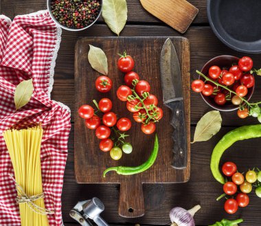 uzun sarı ham spagetti ve kahverengi ahşap bir masa üstten görünüm üzerinde kırmızı kiraz domates