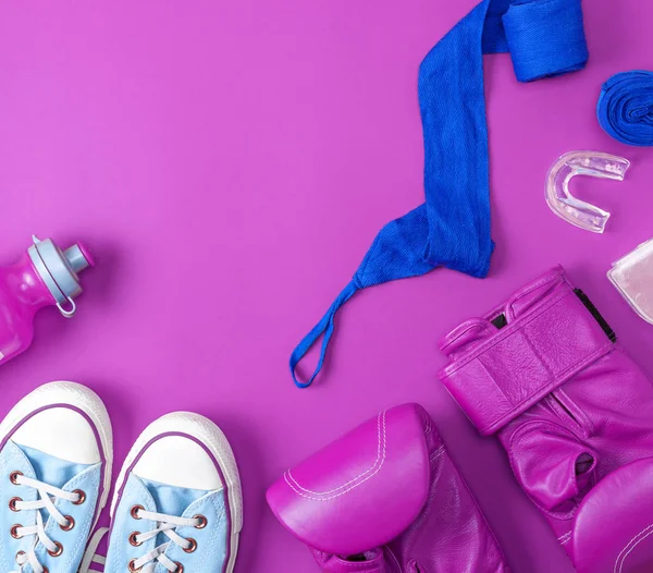 pair of leather pink boxing gloves, a blue textile bandage and a water bottle on a pink background, empty space, abstract sports background