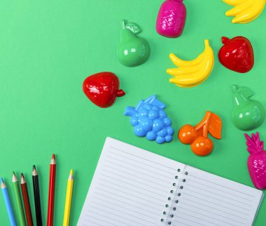 boş beyaz yaprak ve yeşil bir arka planda üstten görünüm çok renkli ahşap kalemler ile not defterini açın