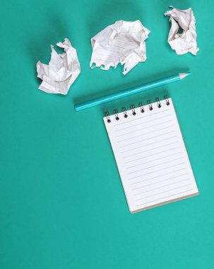 Boş beyaz çarşaflı, buruşmuş kağıt çarşaflı ve yeşil arka planda tahta kalemli bir defter.