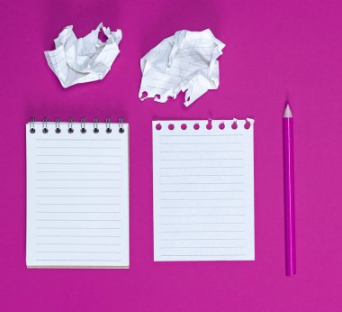 Boş beyaz çarşaflı bir defter, iki buruşmuş kağıt çarşaf ve pembe arka planda ahşap bir pembe kalem.