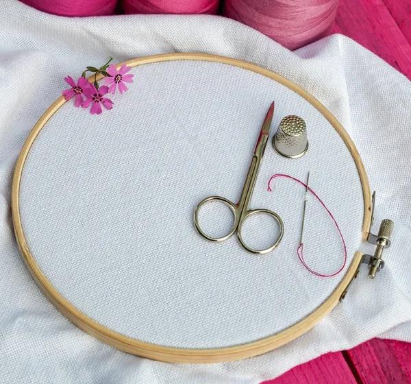 wooden round hoop with white fabric for embroidery and scissors with a thimble, a place for needlework