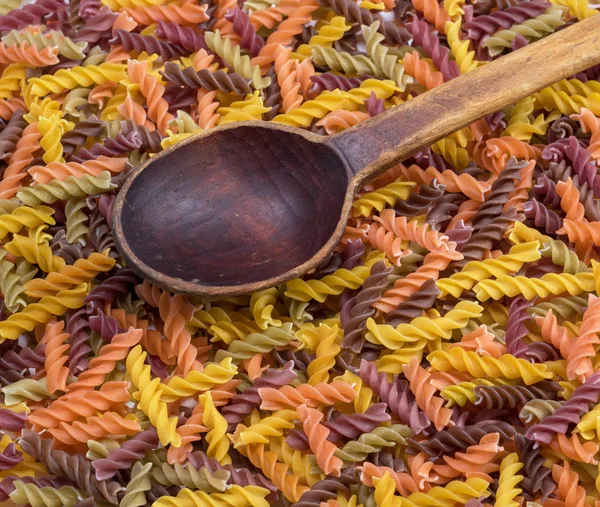 multicolored spiral raw pasta fusilli and empty wooden spoon