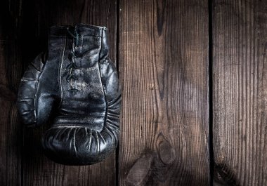 Kahverengi ahşap arka planda bağcıkları olan eski bir deri boks eldiveni sağda boş bir alan.