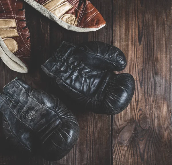 pair of very old leather black boxing gloves with laces and a pair of leather shoes on a brown wooden background, vintage toning