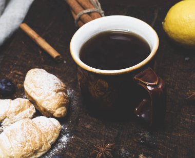 siyah çay ve kruvasan bir ahşap tahta üzerinde kahverengi seramik kupa