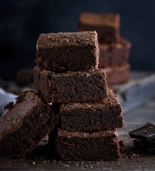 stack of square pieces of baked brown brownie pie on a brown board, a black background