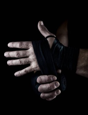man wraps his hands in black textile bandage for sports, black background clipart