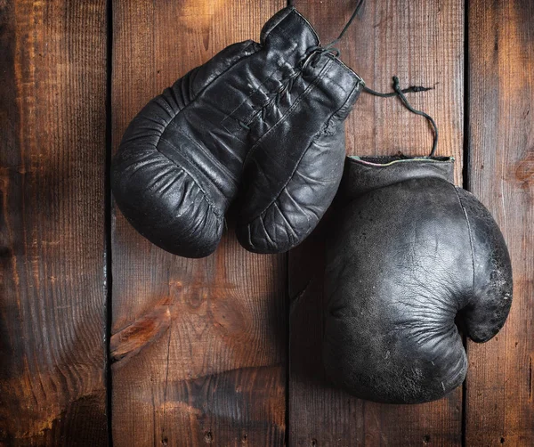 very old black boxing gloves on a brown wooden background, top view