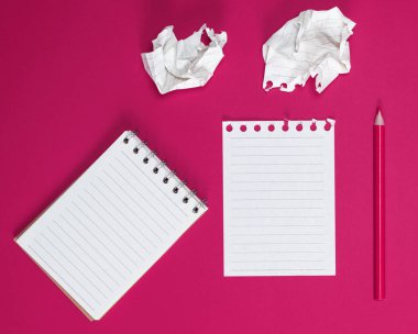 Beyaz çarşaflı ve pembe arka planda buruşmuş bir kağıt parçasıyla açık bir defter.