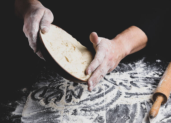 male hand holding a ceramic plate with yeast dough, the cook is preparing to knead the dough